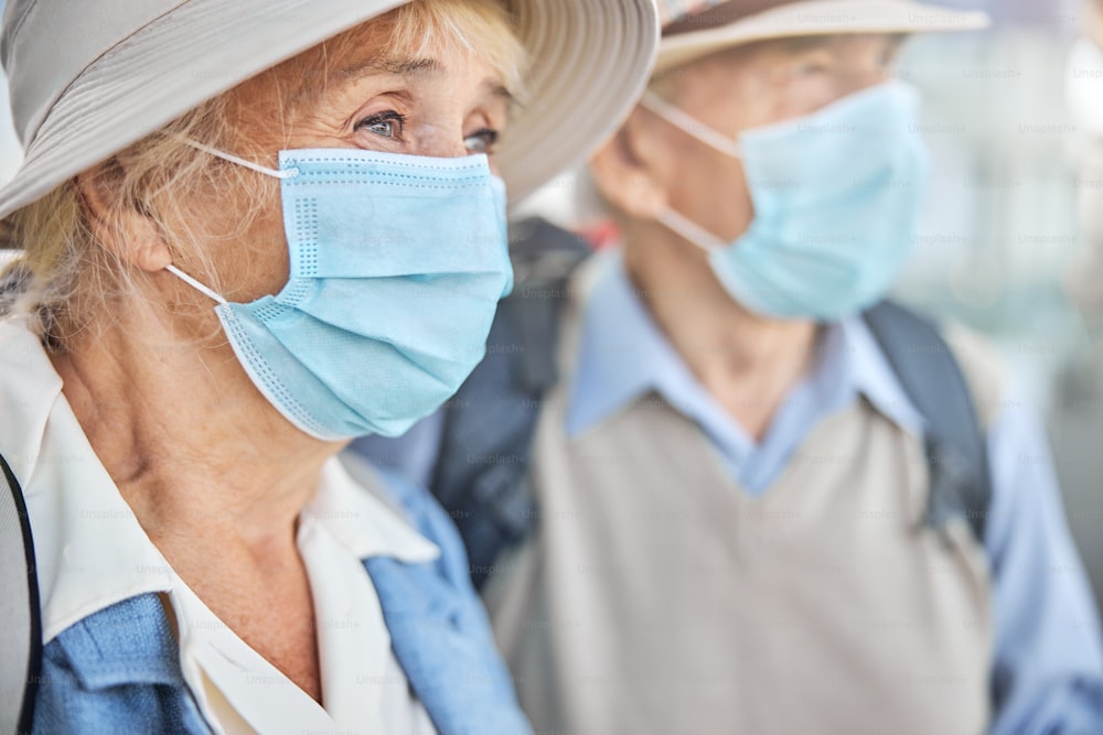 Close up portrait of a senior woman in a face mask and a gray-haired man looking into the distance