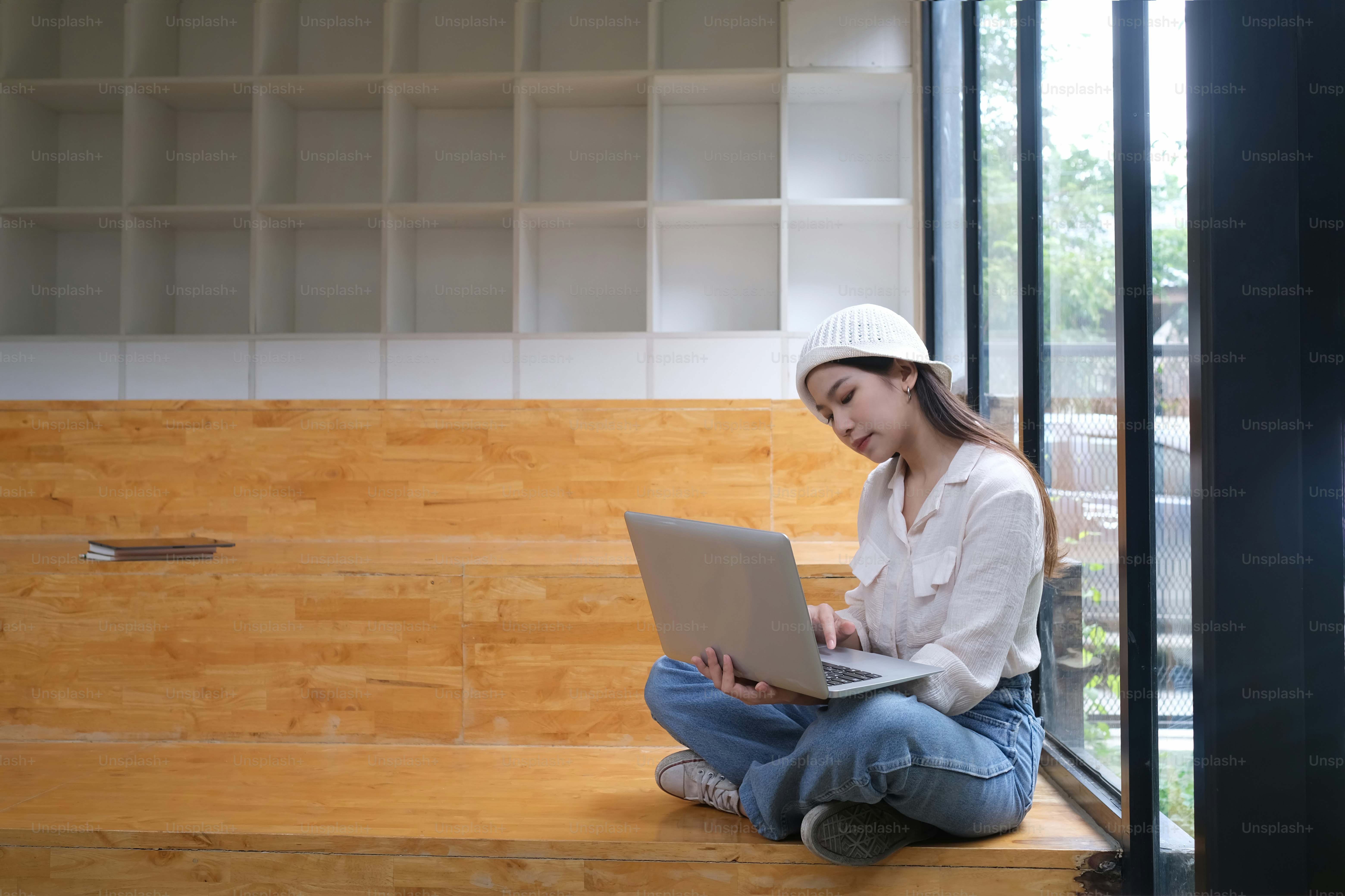 An attractive girl is using a laptop while sitting on the floor.