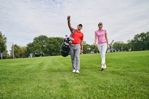 サングラスをかけた女性ゴルファーに何かを見せる中年のゴルフインストラクターの全身肖像画