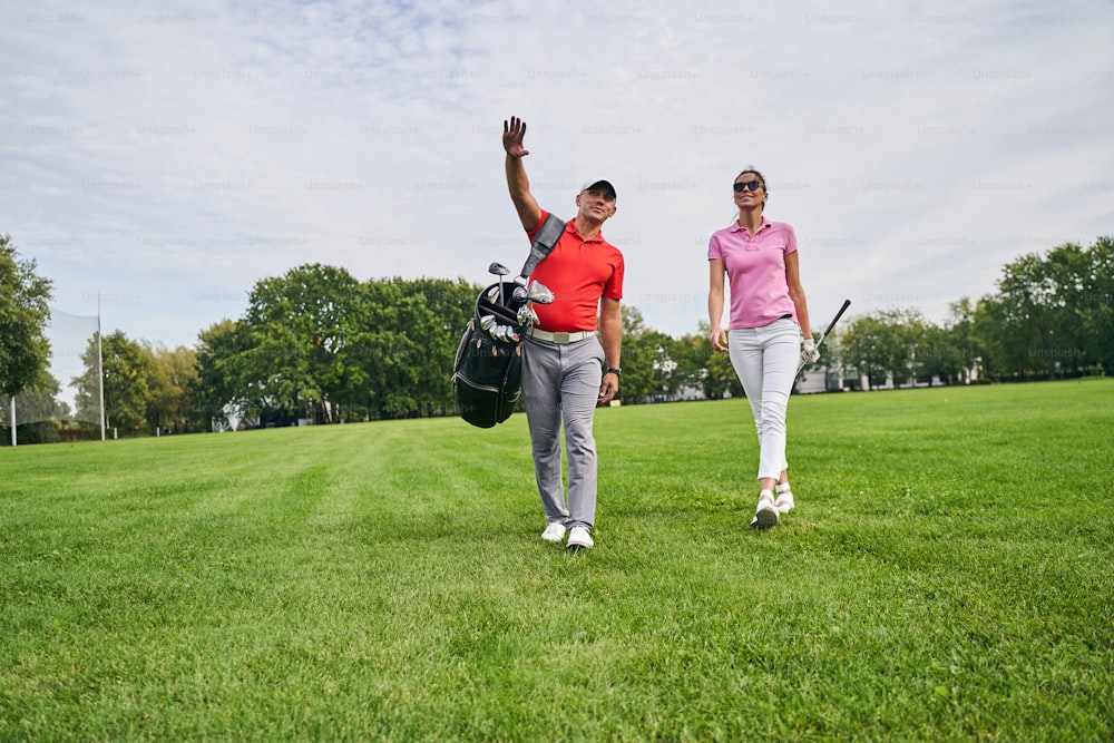Retrato de cuerpo entero de un instructor de golf de mediana edad mostrando algo a una golfista con gafas de sol