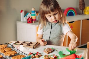 Little girl decorating Christmas gingerbread cookies with sprinkles and chocolate candies. Top view, flat lay.