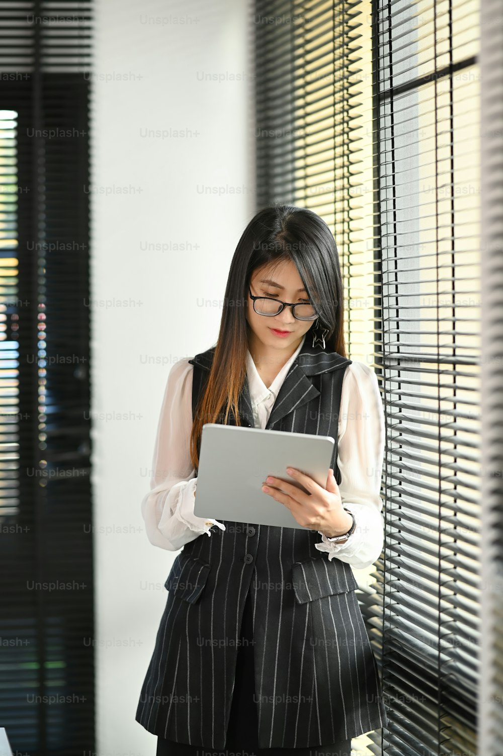 Casual businesswoman with stylus pen writing on digital tablet while standing in modern office.