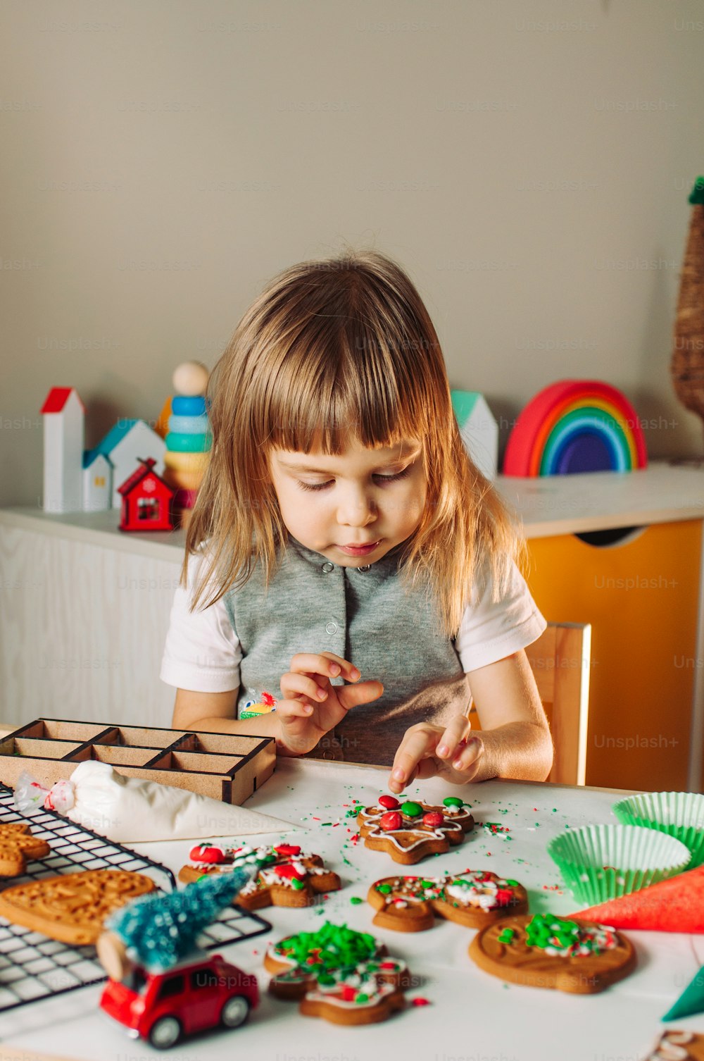 Little girl decorating Christmas gingerbread cookies with sprinkles and chocolate candies.