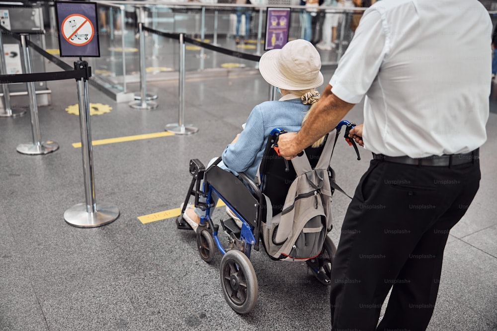 Vista traseira de um funcionário do aeroporto transportando uma viajante deficiente para um avião