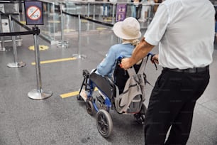 Back view of an airport male employee transporting a disabled female traveler to a plane