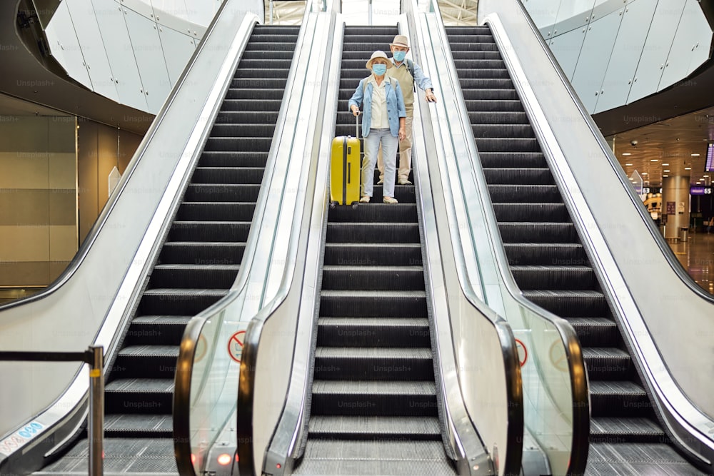 Full-length portrait of a senior couple in face masks using the moving stairs at the airport