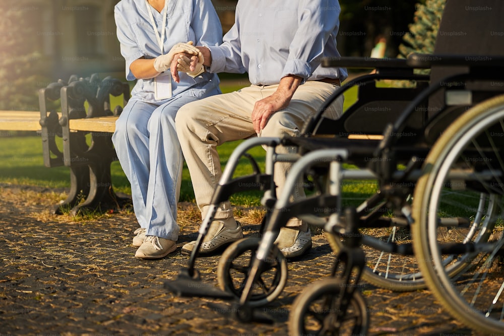 Cropped photo of nurse holding hand of elderly senior patient while sitting on a bench outdoors
