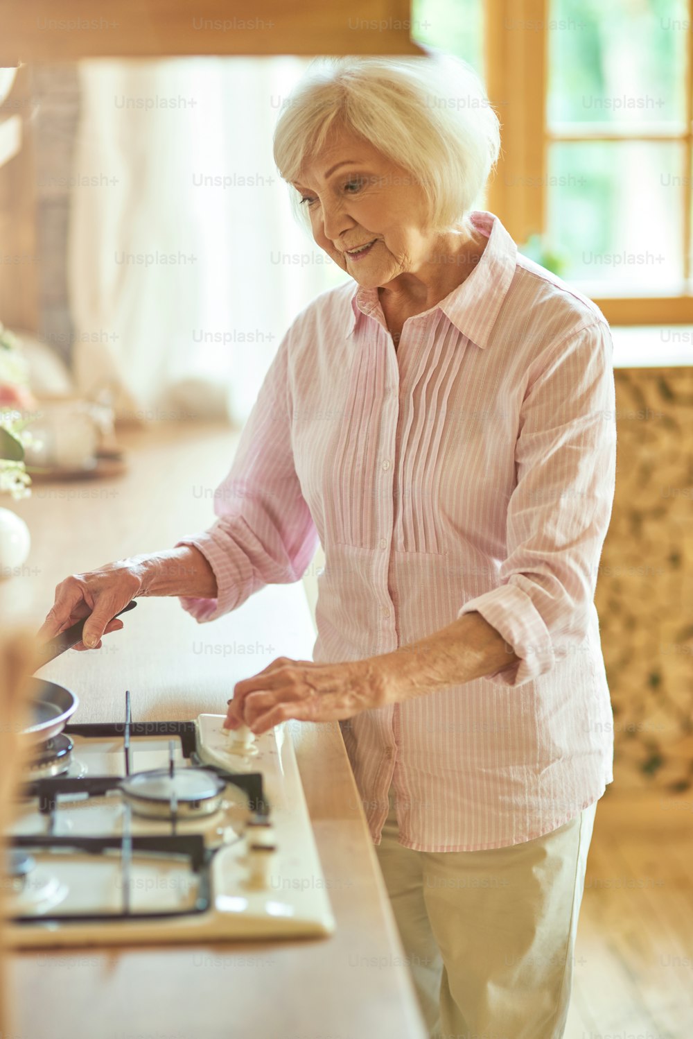 웃는 노인 여자는 스토브를 켜고 집에서 아침 식사를 만들기 위해 프라이팬을 설정합니다. 국내 라이프 스타일 개념