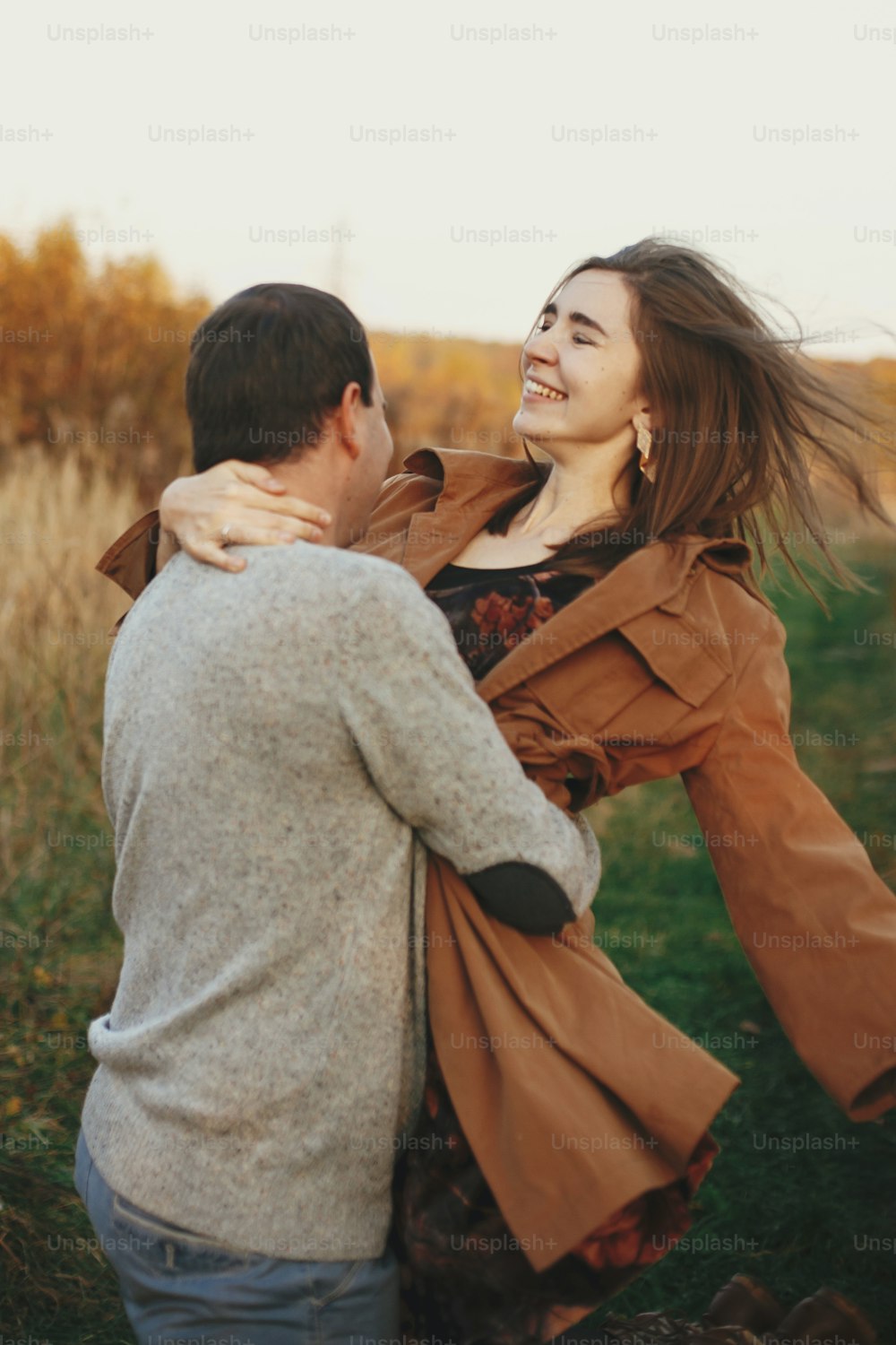 Happy stylish couple dancing in autumn meadow in warm sunset light. Romantic sensual moment. Young emotional woman and man  smiling and whirl in autumn field