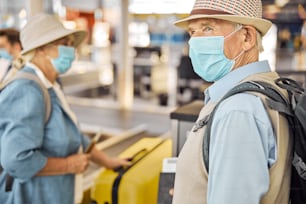 Dos pasajeros con máscaras protectoras colocando su equipaje en la cinta transportadora del aeropuerto