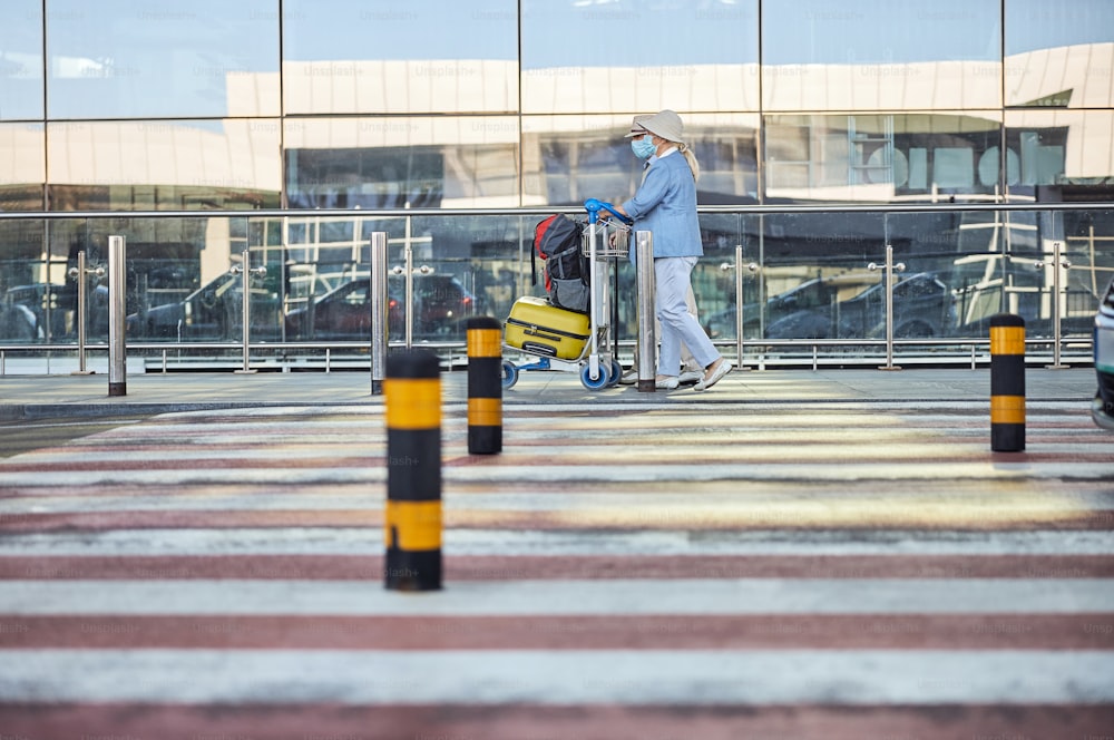 Vista lateral de una turista caucásica de la tercera edad y su marido conduciendo el carrito de equipaje