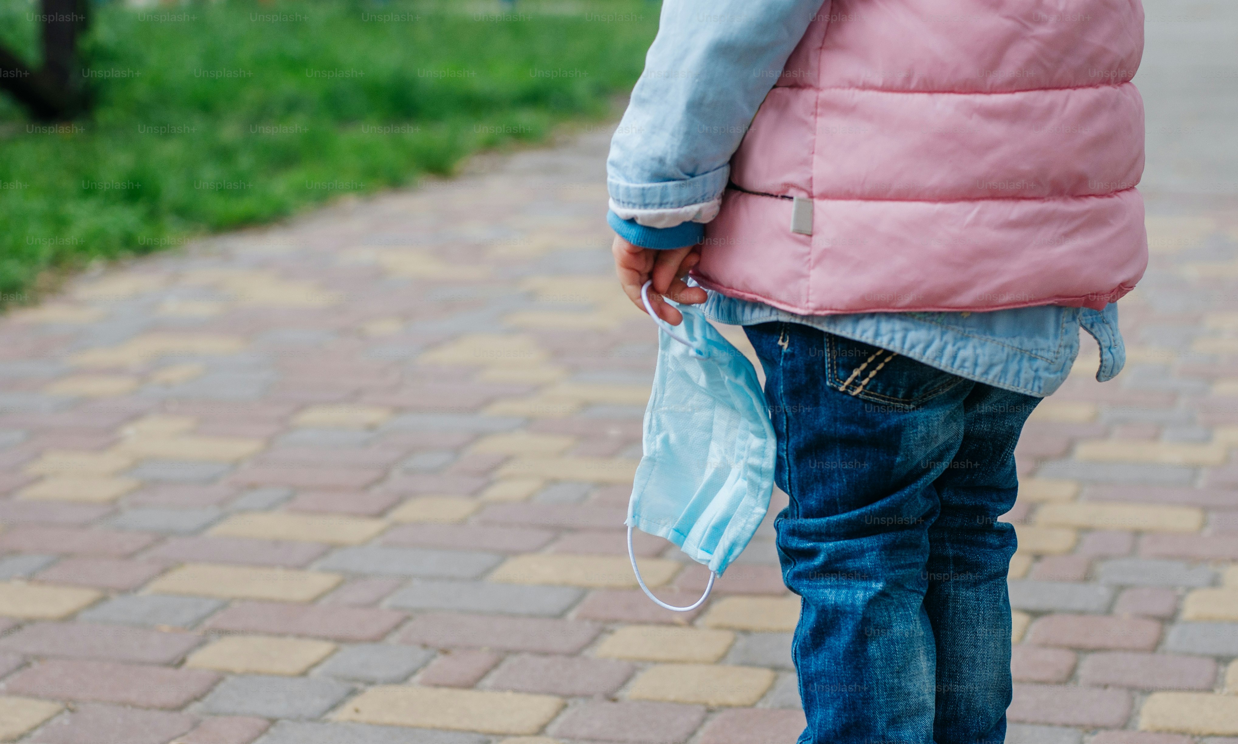 Close up of little girl holding protective face mask outside after the end of quarantine. Pandemic COVID-19 is over concept.