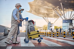 Side view of a man with a walking cane and his spouse with baggage crossing the street