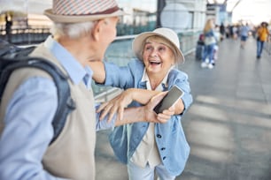 Surprised pleased Caucasian elderly lady reaching out her hands to a man with a cellphone