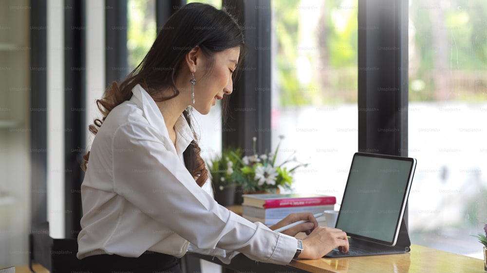 Side view of young businesswoman typing on tablet keyboard in comfortable workspace