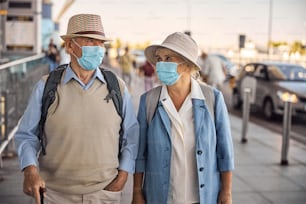 Front view of two senior Caucasian tourists in disposable face masks and hats standing outdoors