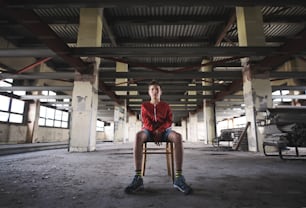 Sad and disappointed teenagers boy sitting on chair indoors in abandoned building.