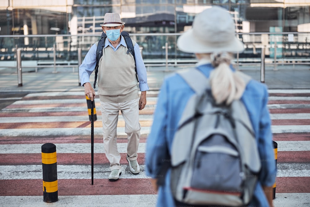 Aged man with a walking cane and a woman with a backpack passing each other