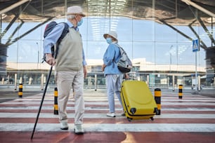 Man with a walking cane and a female tourist with a trolley suitcase staring at each other