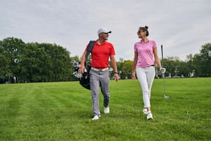 Front view of a smiling lady with a golf club walking next to a professional coach