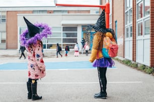 楽しいハロウィンをお過ごし下さい。コスチュームと顔の保護マスクを着た子供たち、女の子、友達が学校に行きます。ハロウィーンの休日を祝う人々の学校の学生。コロナ禍のニューノーマル。