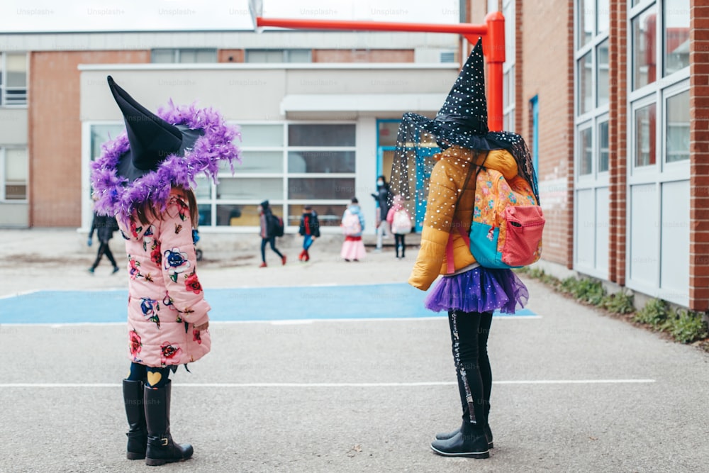 Happy Halloween. Children girls friends in costumes and face protective masks going to school. People school students celebrating Halloween holiday. A new normal during coronavirus.