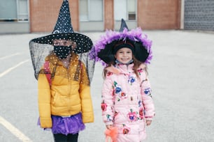 Happy Halloween. Children girls friends in costumes and face protective masks going to school. People school students celebrating Halloween holiday. A new normal during coronavirus.