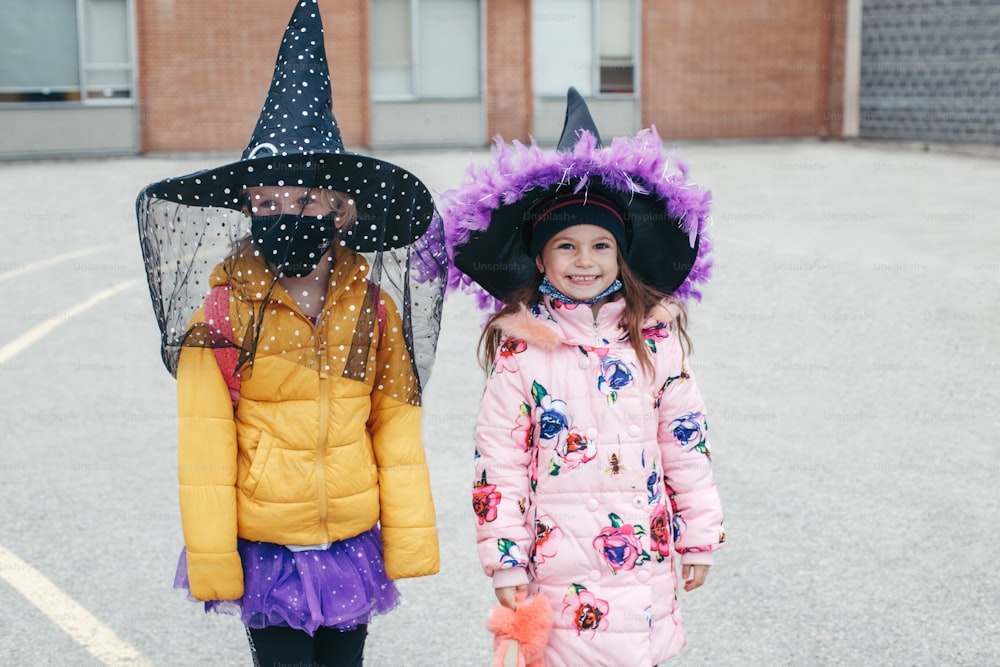 Feliz Dia das Bruxas. Crianças amigas em trajes e máscaras de proteção facial indo para a escola. Pessoas estudantes da escola comemorando feriado de Halloween. Um novo normal durante o coronavírus.