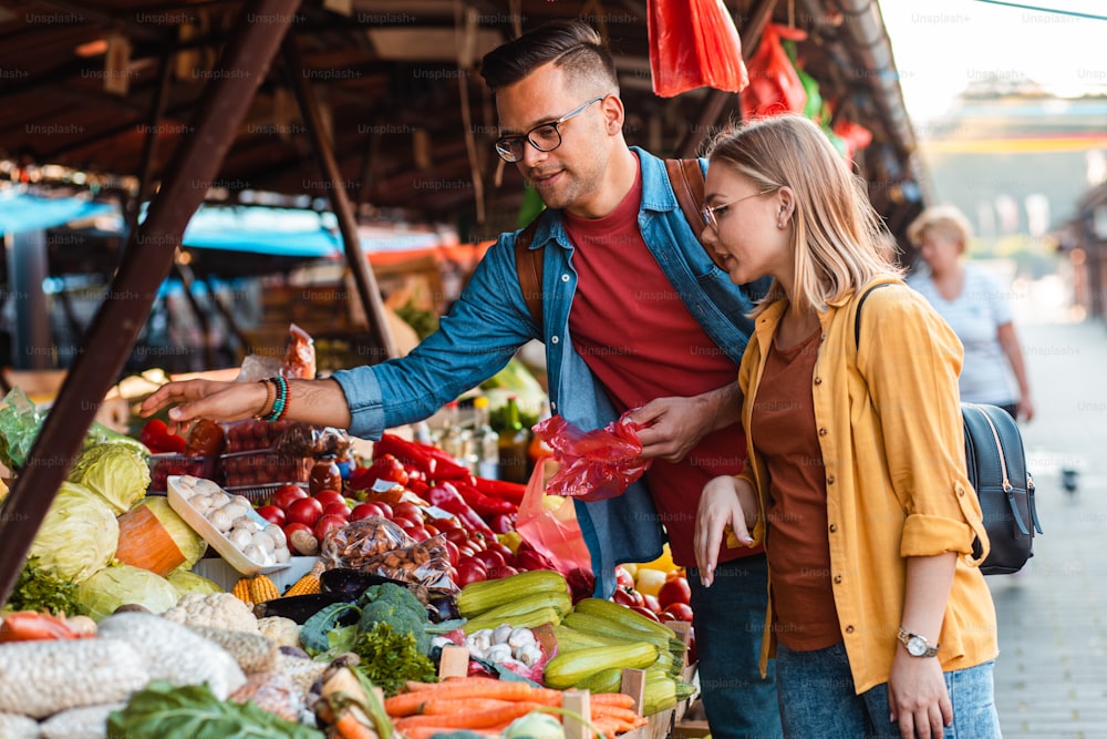 Hermosa pareja joven comprando verduras frescas en el mercado al aire libre.