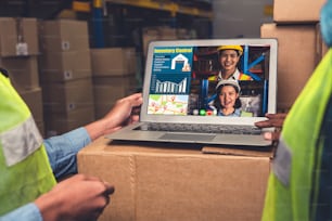 Warehouse staff talking on video call at computer screen in storage warehouse . Online software technology connects people working in logistic factory by virtual conference call on internet network .