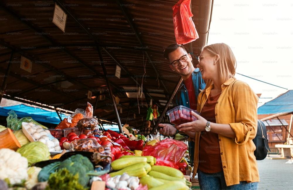 Bella giovane coppia che compra verdure fresche sul mercato all'aperto.