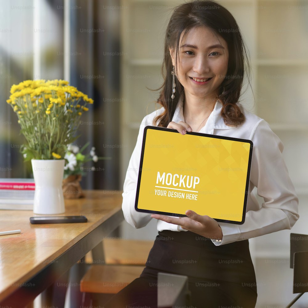 Portrait of young beautiful businesswoman showing her blank screen mock up tablet to the camera and smiling, include clipping path