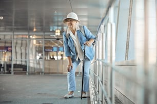 Vista frontal de una turista con un bastón que experimenta un dolor repentino en la rodilla en el aeropuerto