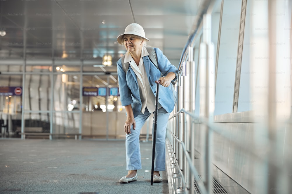공항에서 갑작스러운 무릎 통증을 경험하는 지팡이를 짚은 여성 관광객의 전면 모습