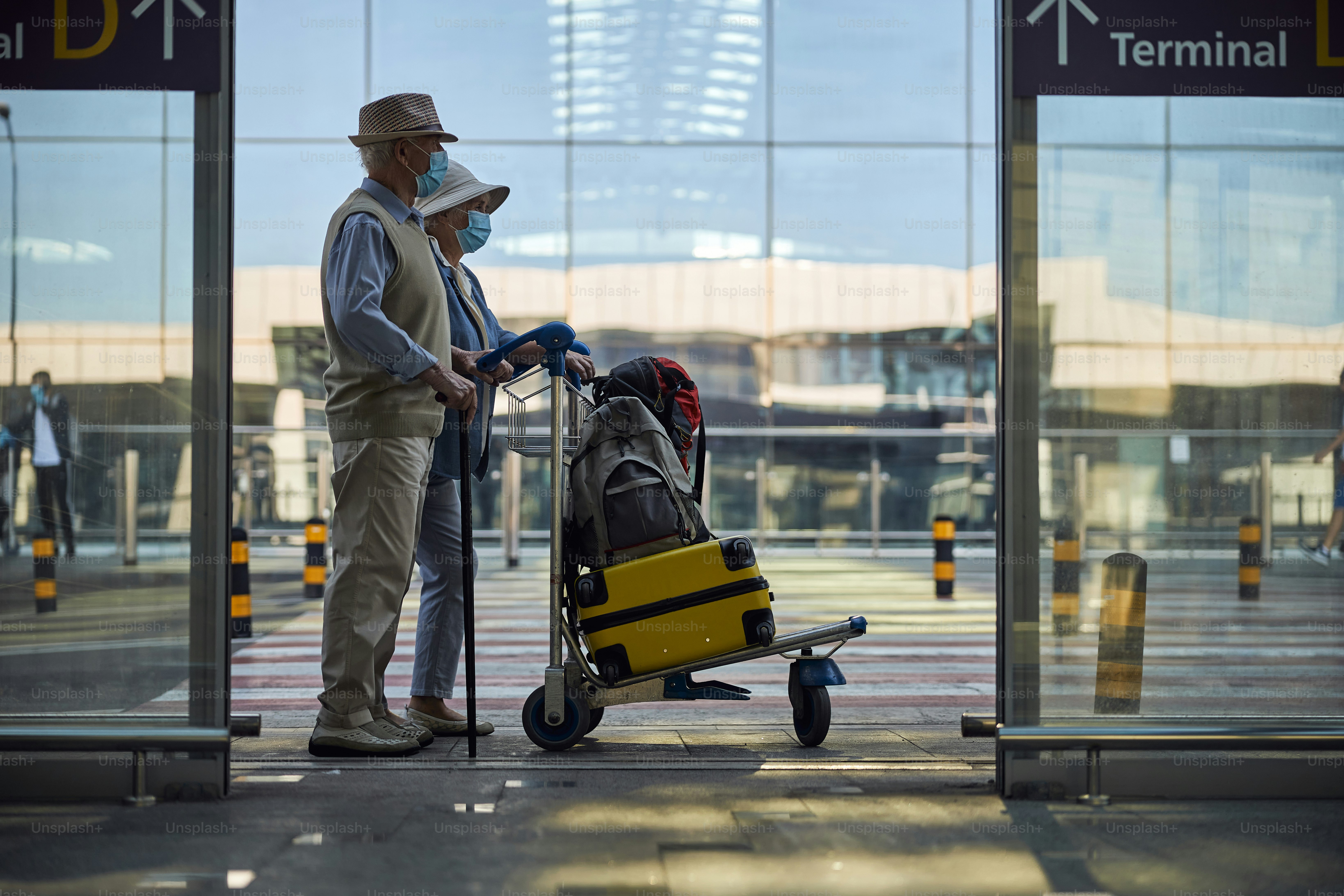 Vista lateral de un turista masculino de edad avanzada y su cónyuge de pie en la entrada de la terminal