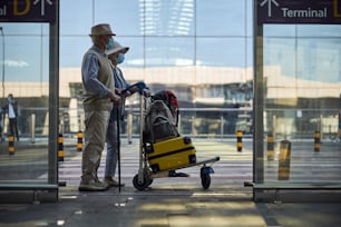 Side view of an aged male tourist and his spouse standing at the terminal entrance