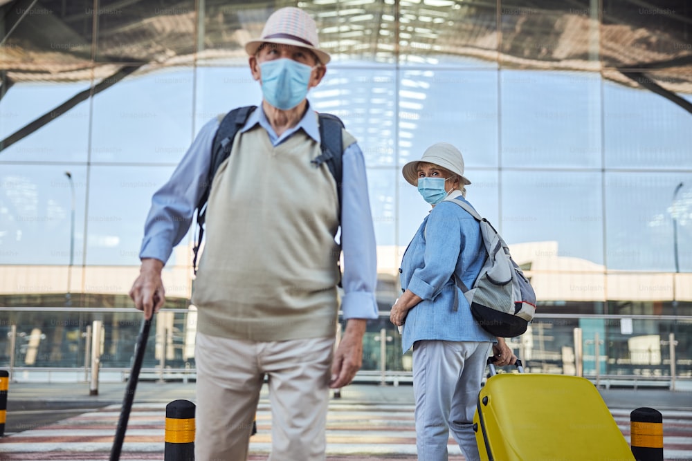 Turista anziana in una maschera facciale che fissa un uomo con un bastone da passeggio