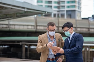 Two Businessman colleague wearing protective face mask discussing business project with using digital tablet in the city