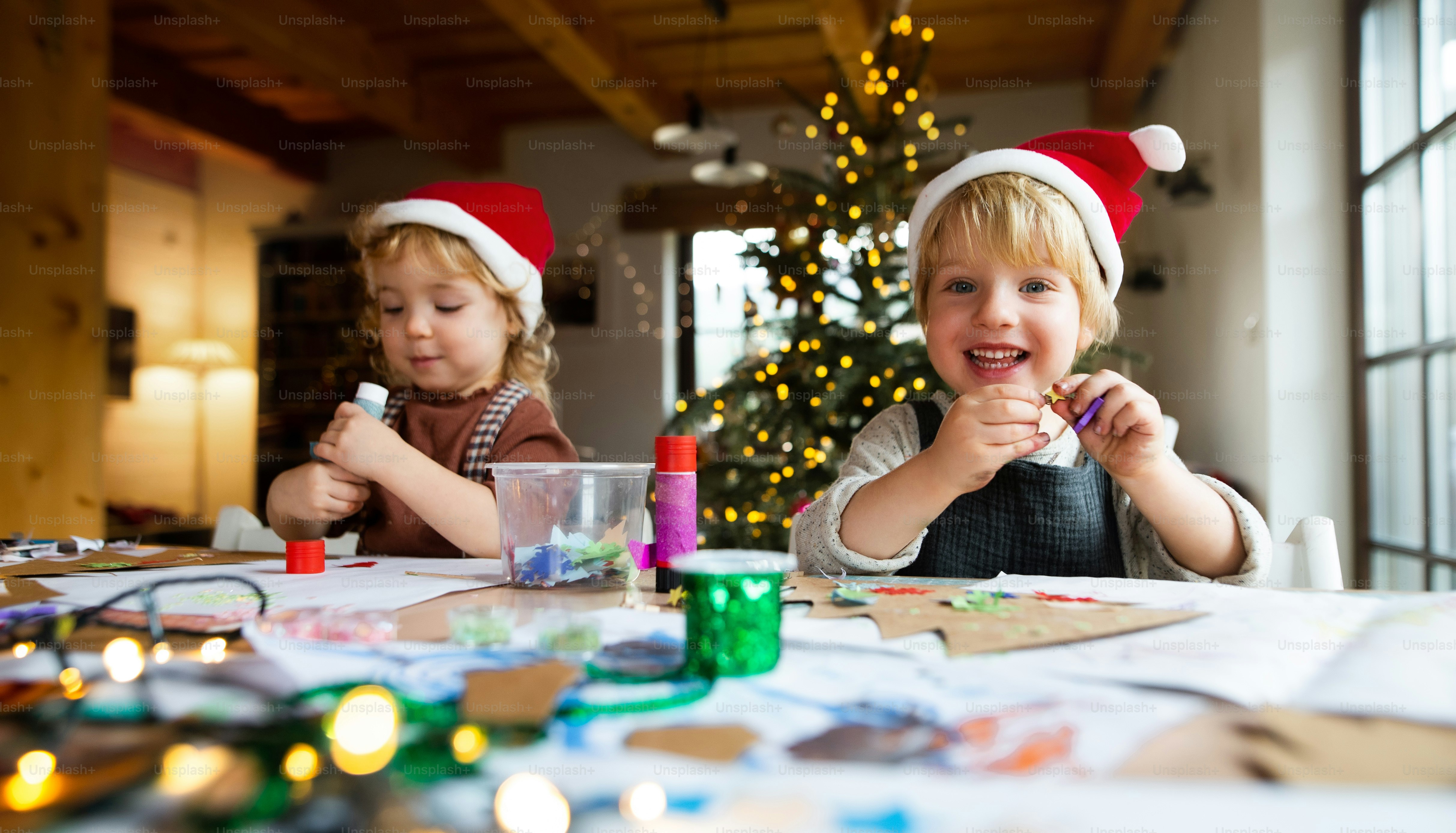 Retrato de niña y niño felices en el interior de casa en Navidad, haciendo arte y artesanía.