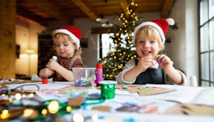 Portrait of happy small girl and boy indoors at home at Christmas, doing art and craft.