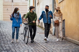 Group of young people with bicycle outdoors in town, walking and talking. Coronavirus concept.