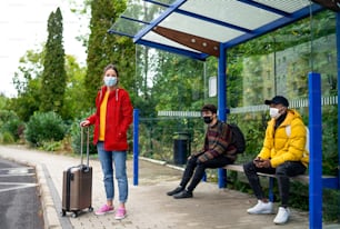 Young people on bus stop outdoors in town. Coronavirus and safe distance concept.