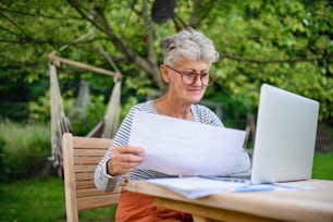 Mujer mayor activa con computadora portátil que trabaja en la mesa al aire libre en el jardín, concepto de oficina en casa.