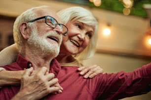 Lächelndes älteres Ehepaar, das Händchen hält, während es abends im Freien gemeinsam Selfies macht. Lifestyle-Konzept