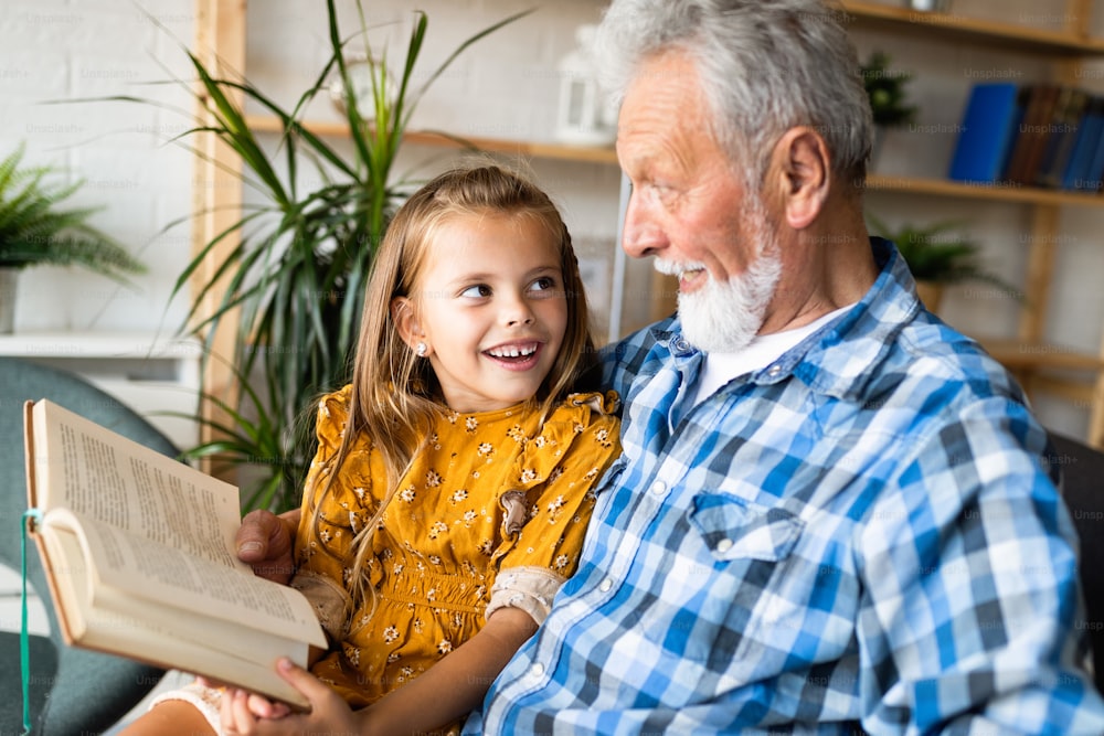 Happy little girl with cute grandfather reading story book at home