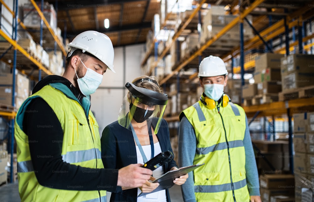 A group of workers with manager working indoors in warehouse, coronavirus concept.