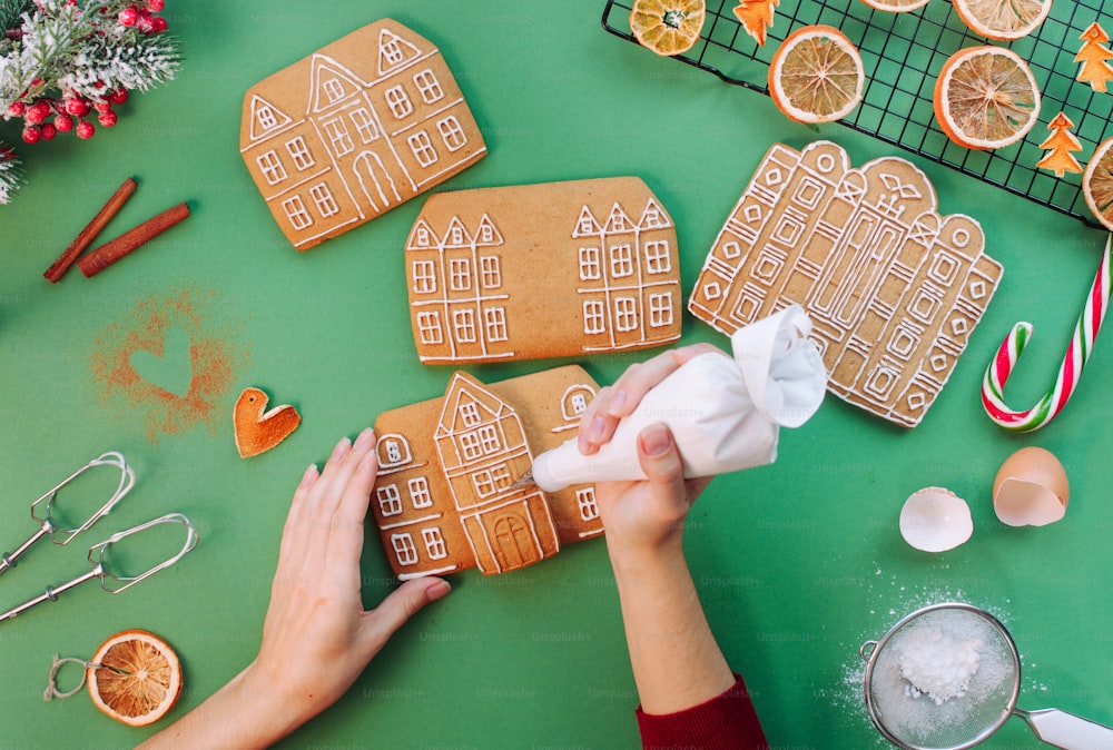 Female hands decorating Christmas gingerbread cookies house. Top view, flat lay.
