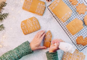 Female hands decorating Christmas gingerbread cookies houses. Top view, flat lay.