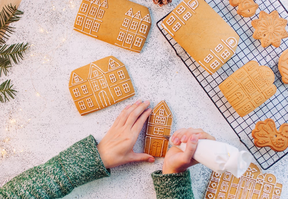 Female hands decorating Christmas gingerbread cookies houses. Top view, flat lay.