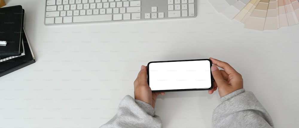 Cropped shot of young woman hand holding horizontal blank screen mobile phone on her work space.